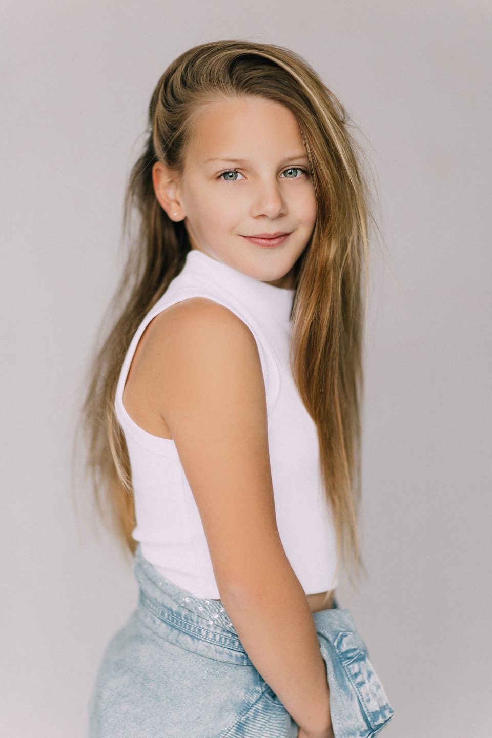 Smiling girl with long blonde hair in a white top posing for a modelling shoot